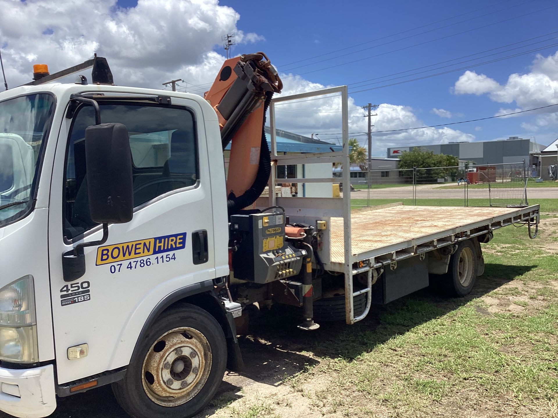 White Flatbed Truck With a Mounted Crane Parked on Grass Under a Cloudy Sky — Bowen Hire in Bowen, QLD