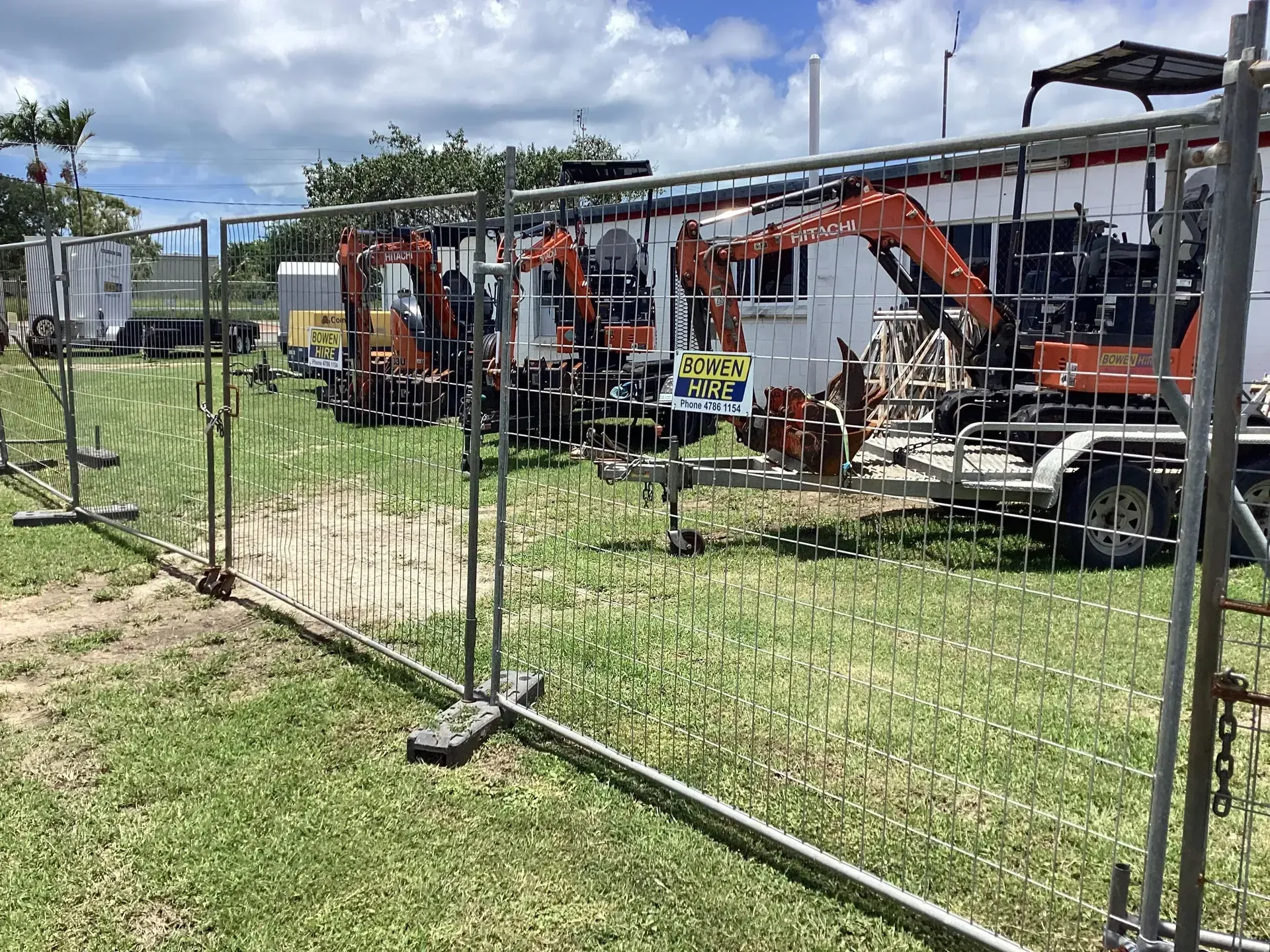 Construction Equipment Lined up Behind a Metal Fence — Bowen Hire in Collinsville, QLD