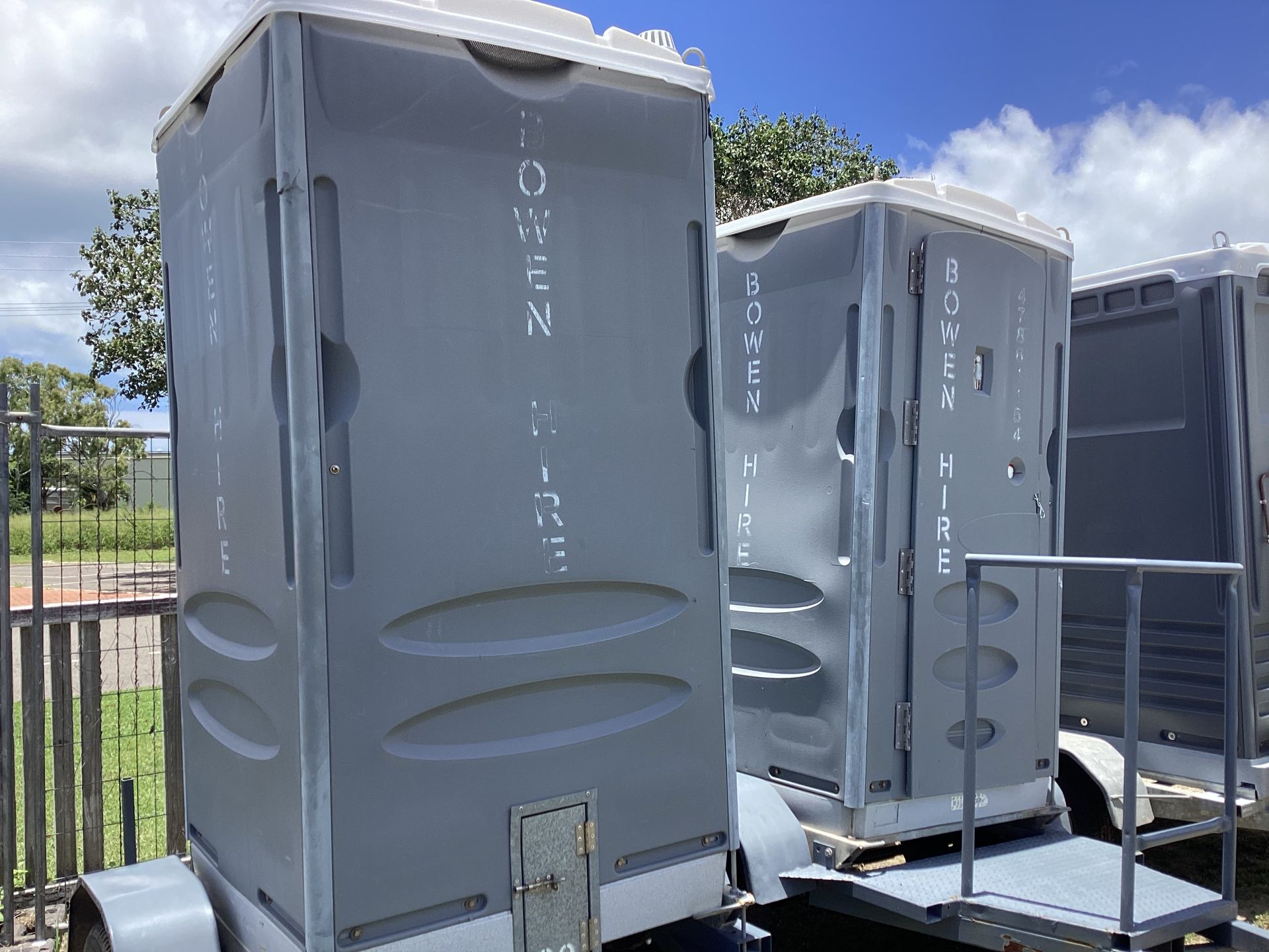 Gray Portable Toilets Lined Up Outdoors on a Sunny Day — Bowen Hire in Bowen, QLD