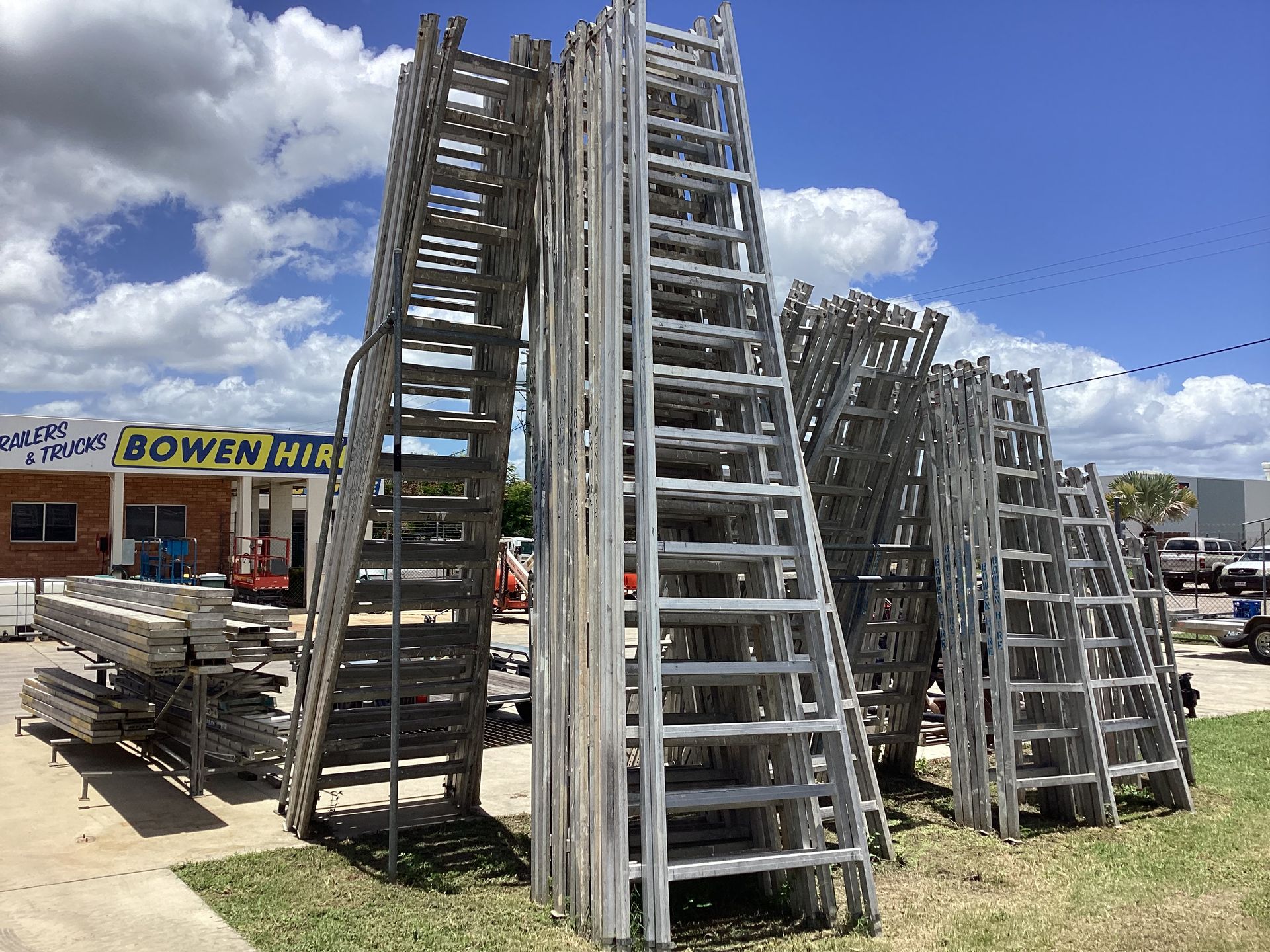 Stacks of Aluminum Ladders Outside a Hardware Store Under a Blue Sky With Clouds — Bowen Hire in Bowen, QLD