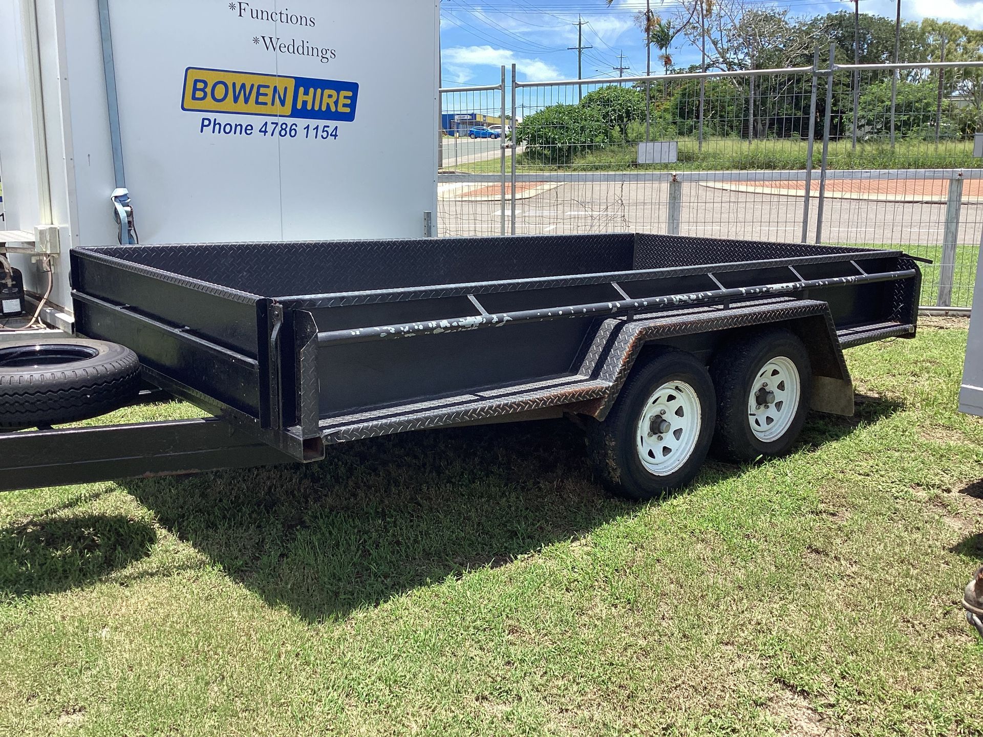 Black Utility Trailer Parked on Grass Beside a Building and Fence — Bowen Hire in Bowen, QLD