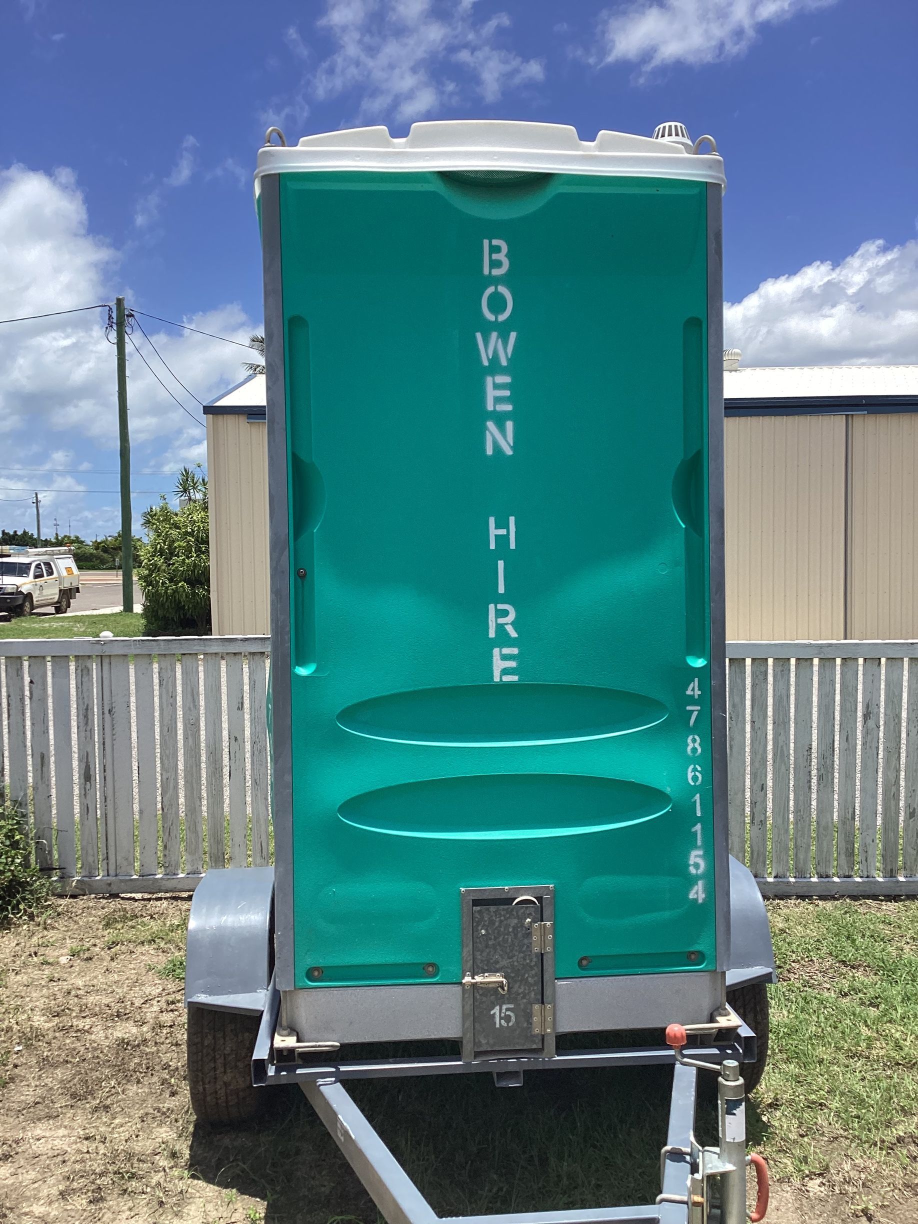 Turquoise Portable Toilet Labeled Bowen Hire on a Trailer in a Grassy Yard — Bowen Hire in Bowen, QLD