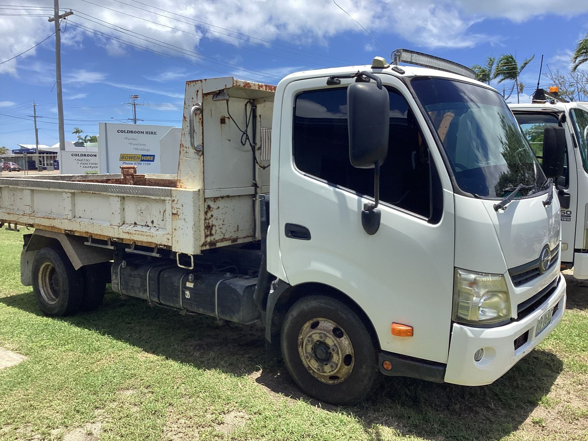 A White Dump Truck Parked on a Grassy Lot Under a Sunny Blue Sky — Bowen Hire in Bowen, QLD