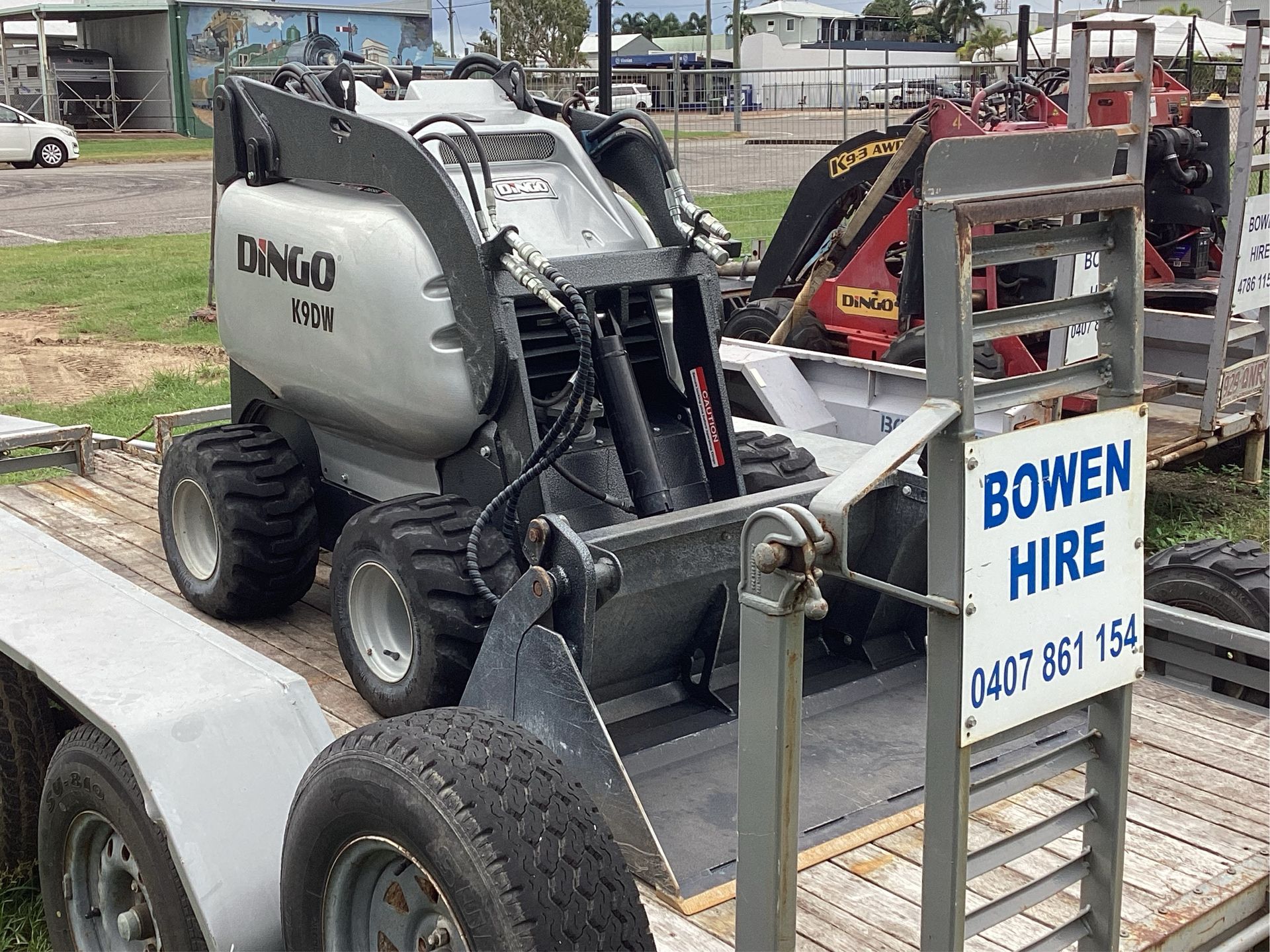 Bobcat Skid Steer on Trailer Beside Bowen Hire Sign in a Yard — Bowen Hire in Bowen, QLD