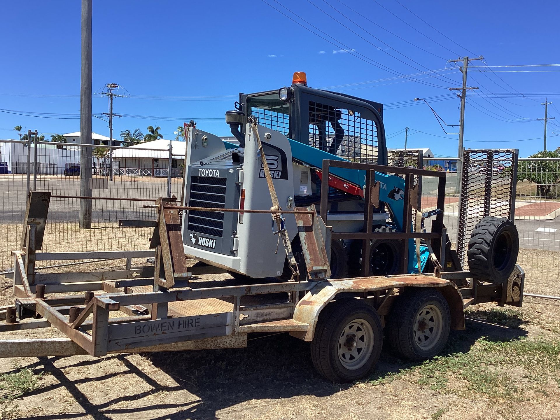 Small Skid Steer Loaded on a Flatbed Trailer in a Fenced Outdoor Lot Under a Blue Sky — Bowen Hire in Bowen, QLD