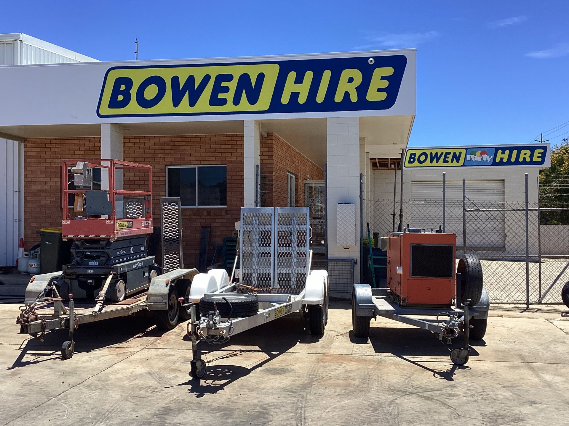Bowen Hire Equipment Yard With Trailers and Machinery in Front of a Blue Sign and Building — Bowen Hire in Bowen, QLD