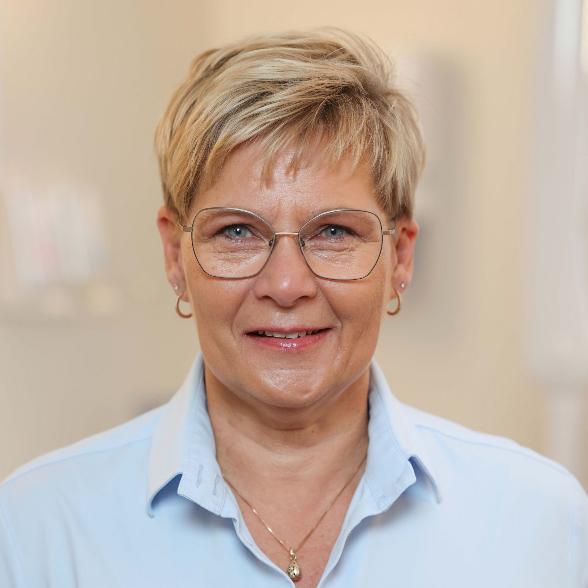 En kvinde med briller og blå skjorte smiler til kameraet.