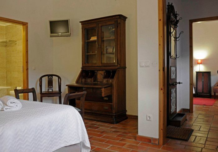 Quarto com escrivaninha antiga, cadeiras e porta para o banheiro. Piso de tijolos vermelhos.