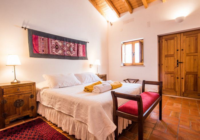 Quarto com cama branca, móveis de madeira e um banco vermelho, sob um teto inclinado.