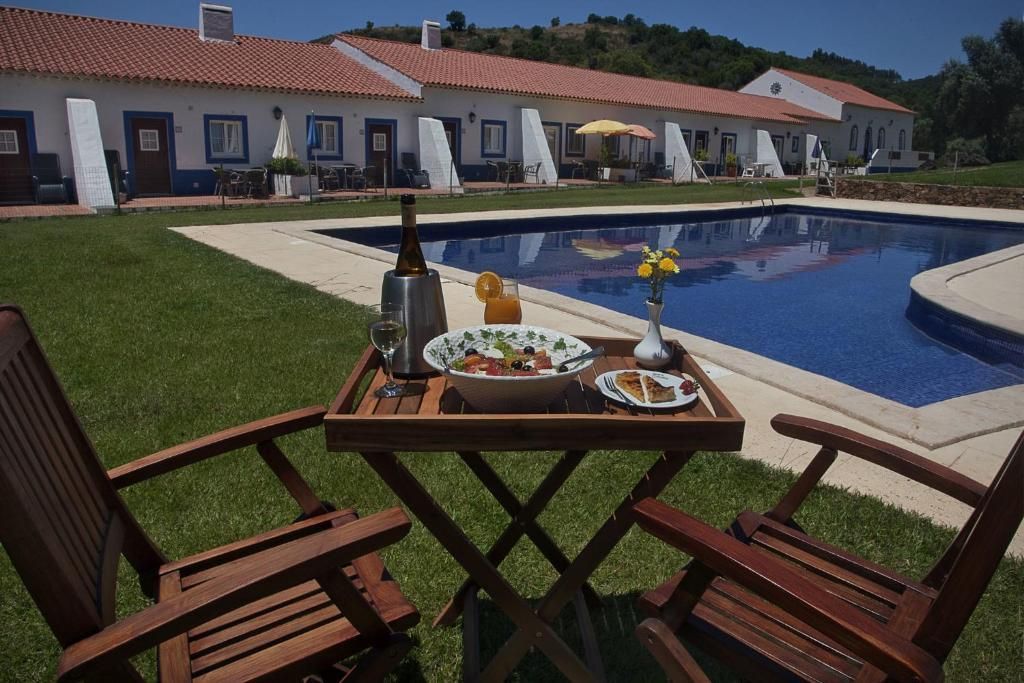 Área de jantar ao ar livre junto à piscina em um resort com edifícios brancos e telhados de telha vermelha.