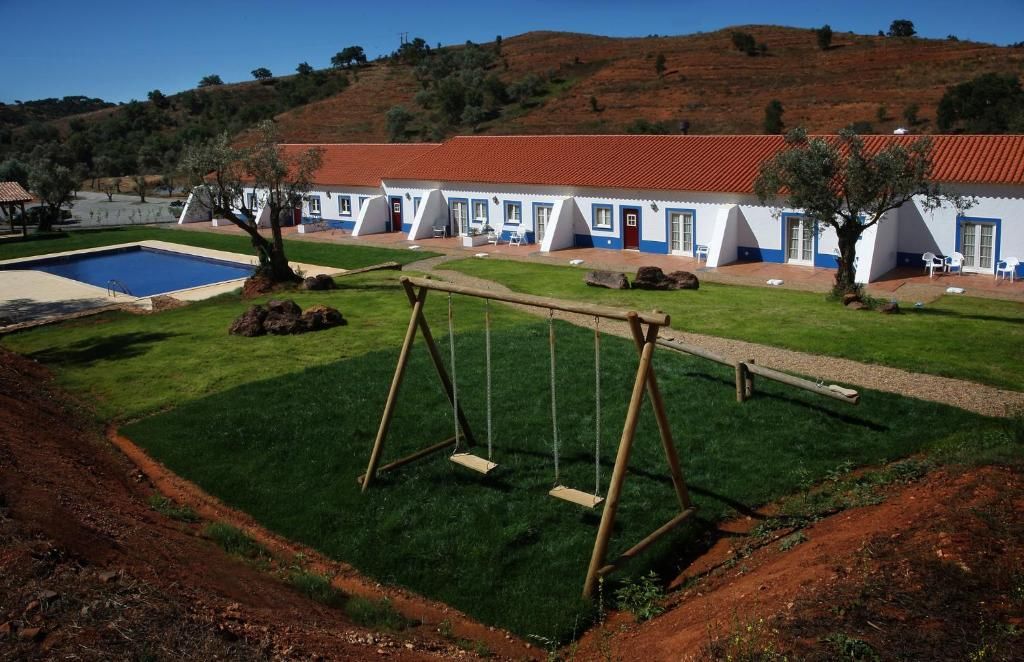 Uma fileira de prédios brancos com detalhes em azul e telhados vermelhos, um balanço e uma piscina em um gramado verde.
