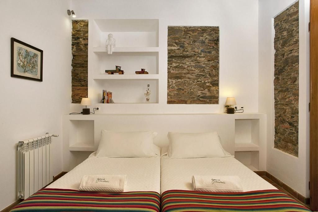 Quarto com duas camas de solteiro, paredes brancas, detalhes em pedra e prateleiras embutidas.