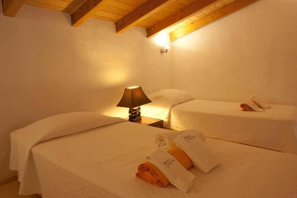 Duas camas em um quarto de paredes brancas com teto de madeira. Um abajur fica entre as camas, com toalhas dobradas sobre elas.
