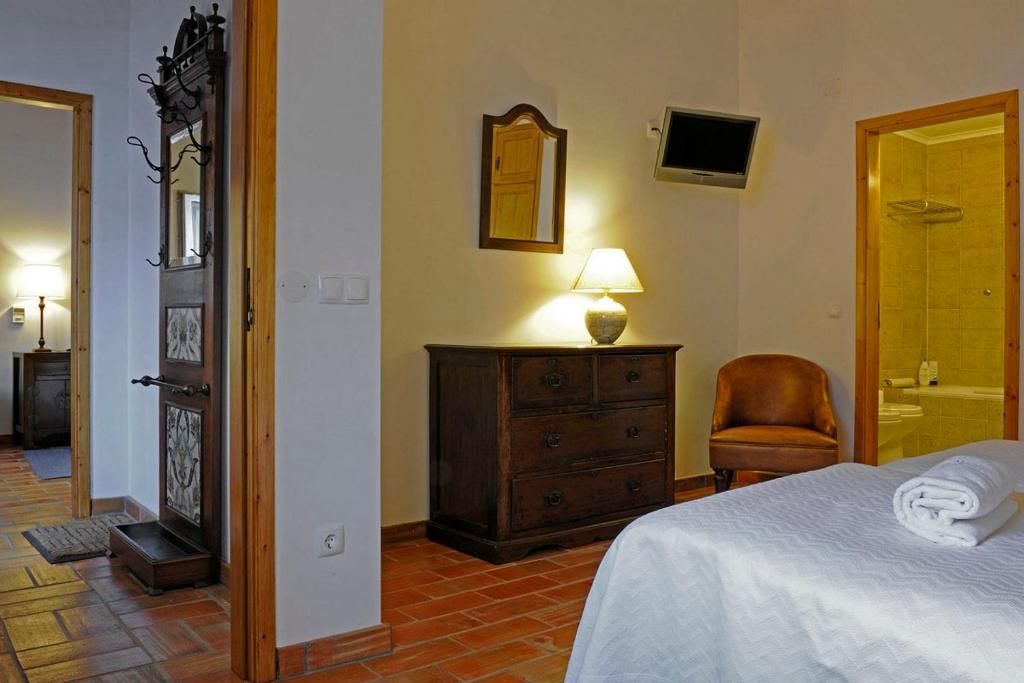 Quarto com móveis de madeira, piso de ladrilho de terracota e porta aberta para outro cômodo.