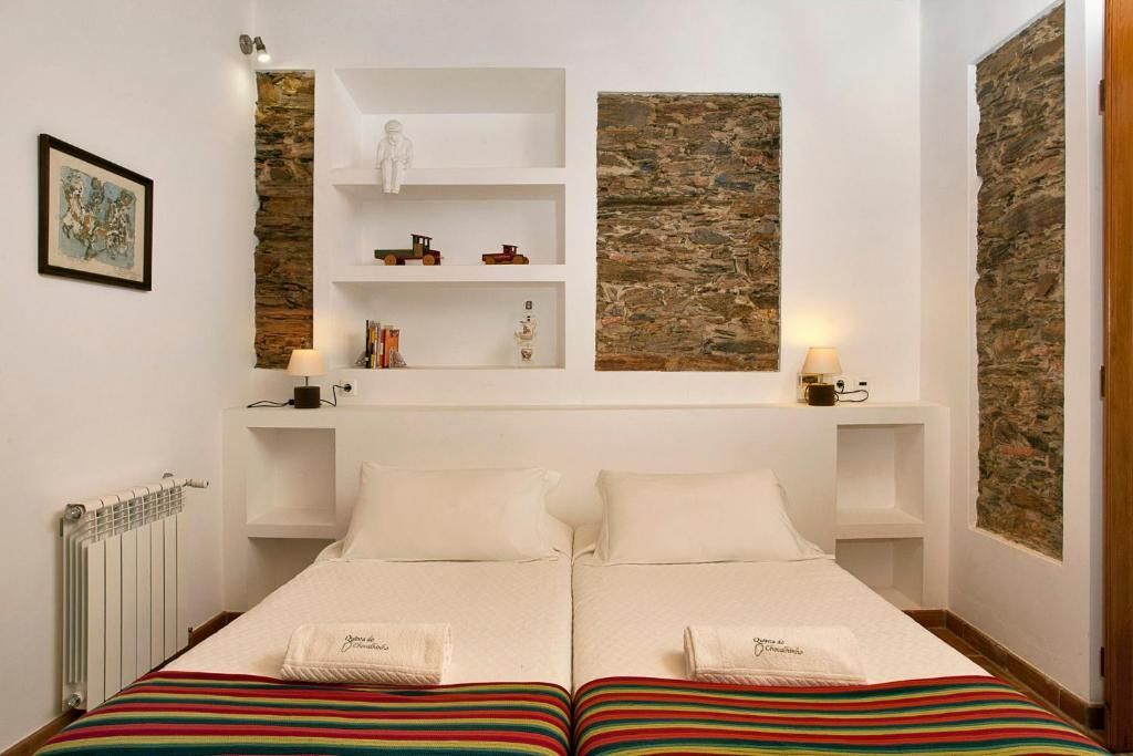Quarto com duas camas de solteiro, detalhes em pedra nas paredes, prateleiras brancas, obras de arte e radiador.