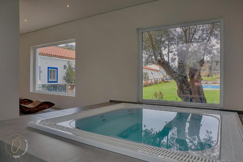 Spa interno com grandes janelas com vista para um gramado verde e uma árvore, com um vislumbre de uma casa ao longe.