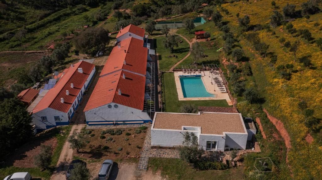 Vista aérea de edifícios brancos com telhados laranja, piscina, jardim verde e colinas circundantes.