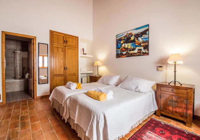 Quarto com duas camas de solteiro, móveis de madeira, obras de arte e banheiro privativo.