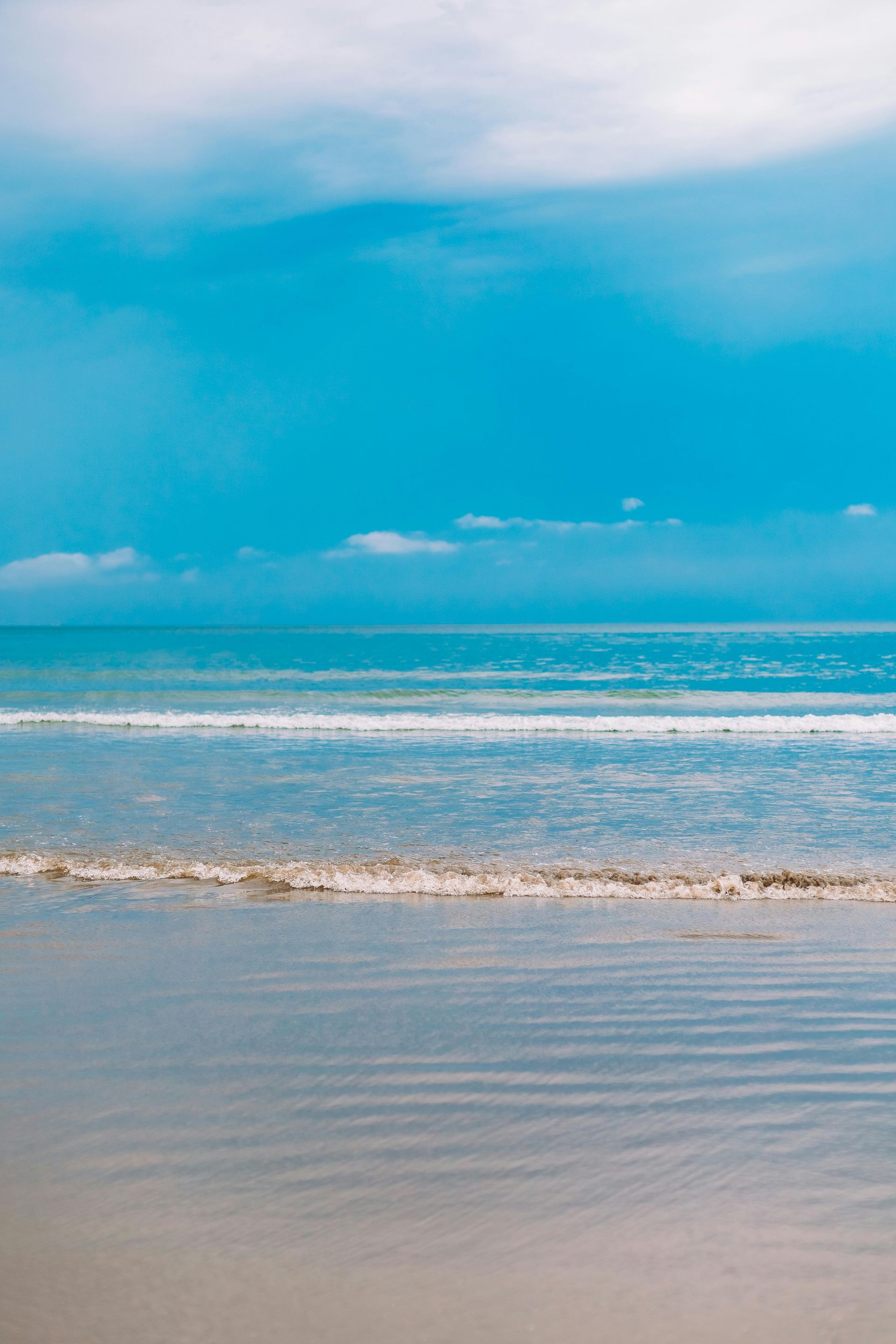 Cena de praia com céu azul, oceano e ondas suaves a banhar a costa.