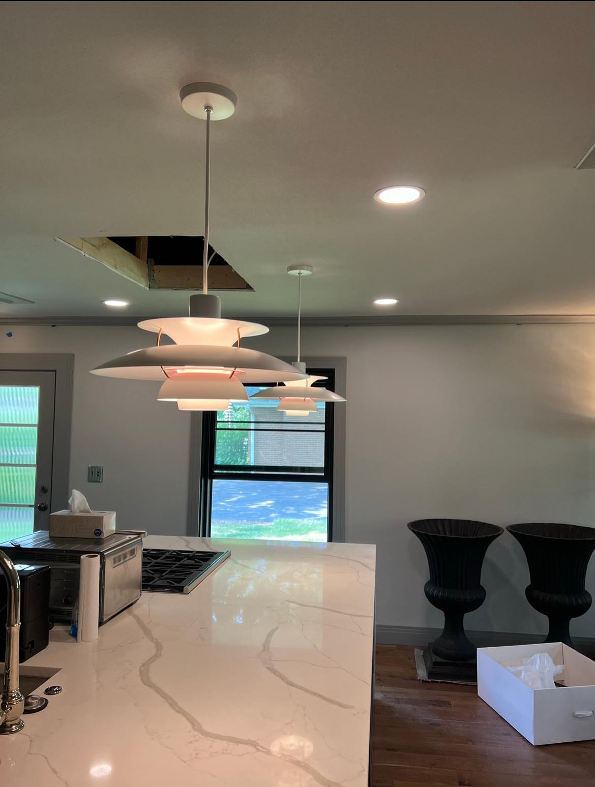 Kitchen with overhead pendant lights, white countertops, a black window, and a hole in the ceiling.