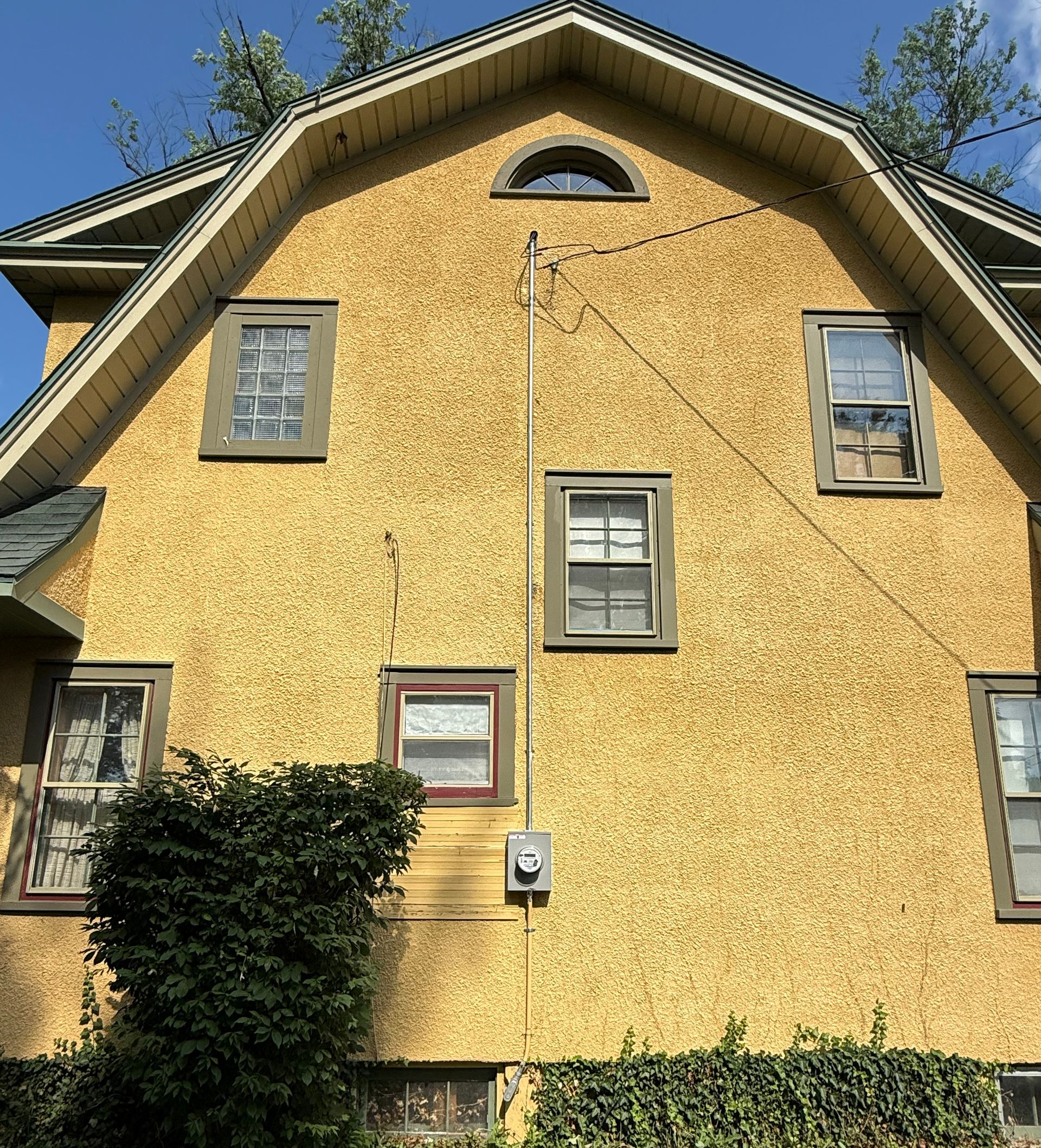 Yellow stucco house with multiple windows; electrical conduit runs up the side.