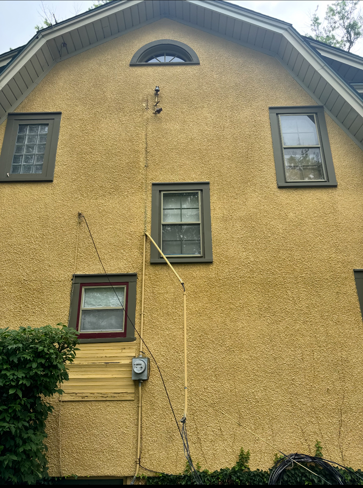 Yellow stucco house with windows and electrical wiring running down the side.