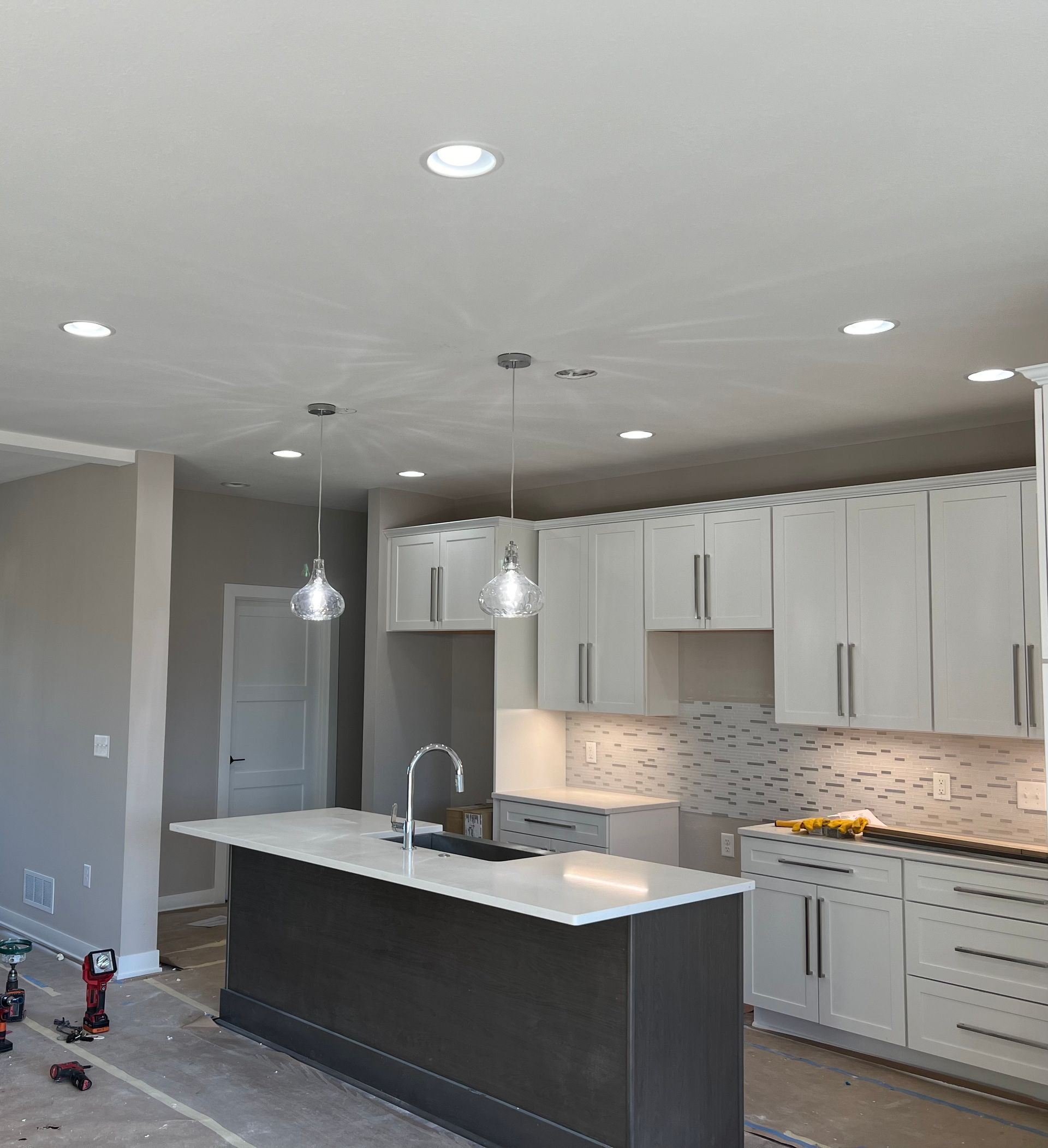 Modern kitchen under construction with island, white cabinets, and pendant lights.