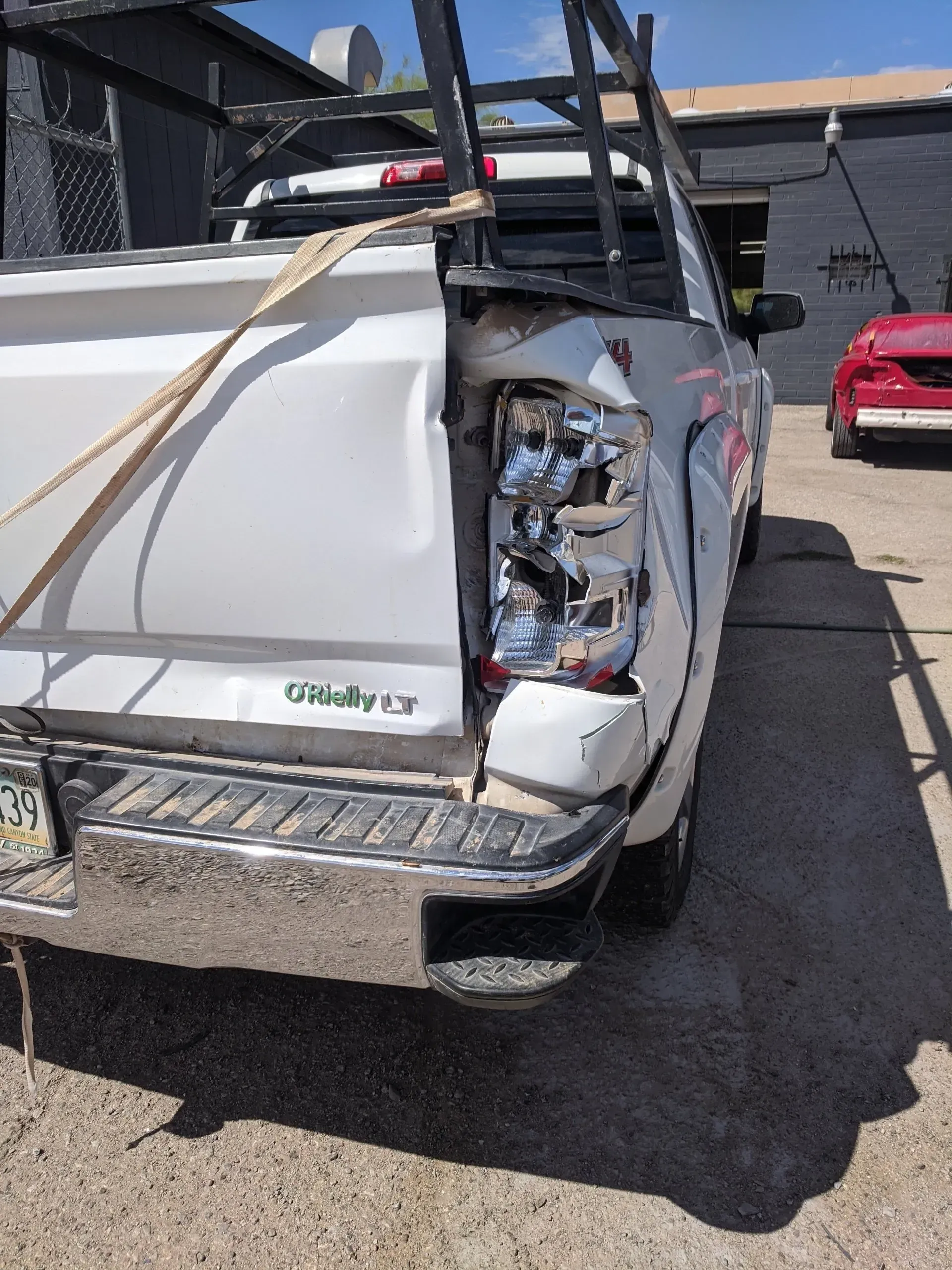 A white truck with a broken tail light is parked in a parking lot.