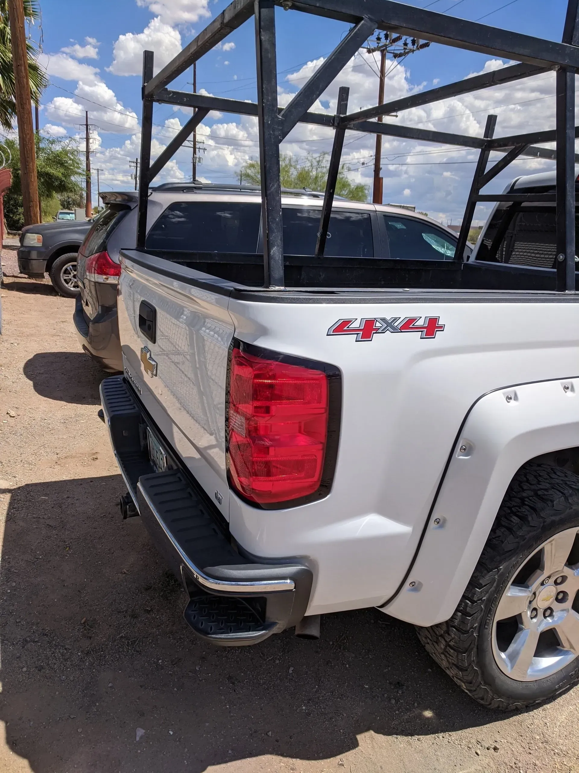 A white truck with a ladder rack on the back is parked in a dirt lot.