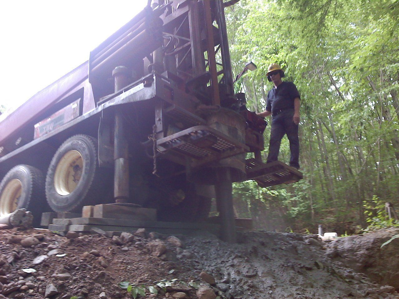 Drilling rig and worker in a forest. Muddy ground.