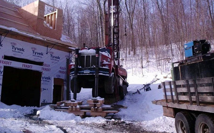 A red drilling rig next to a building under construction, in a snowy wooded area.