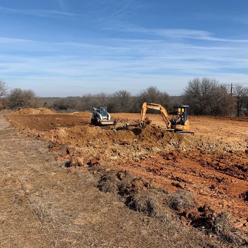 Bulldozer and excavator grading a dirt lot under a blue sky
