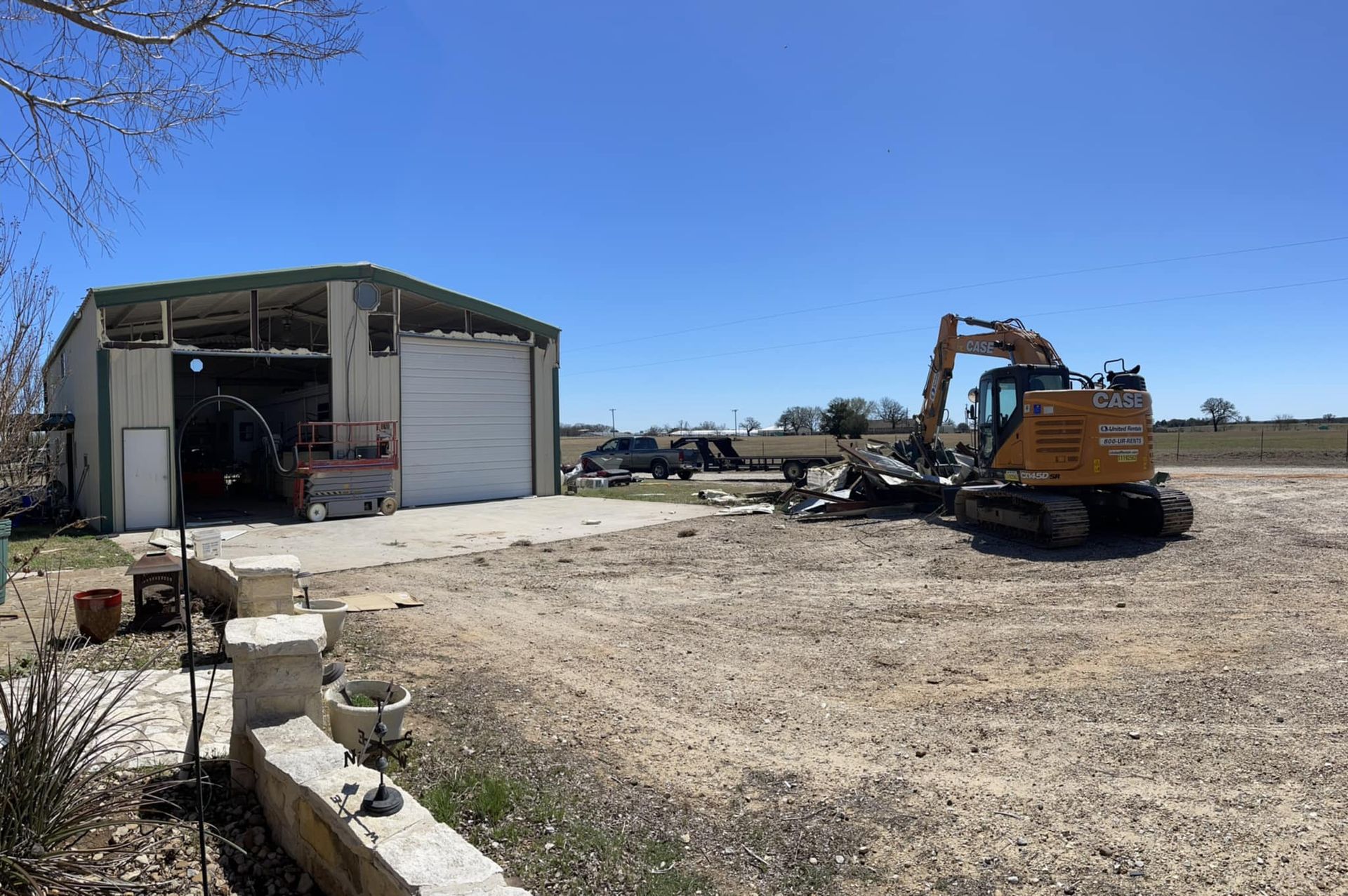 Construction equipment beside an open metal shed on a sunny dirt lot