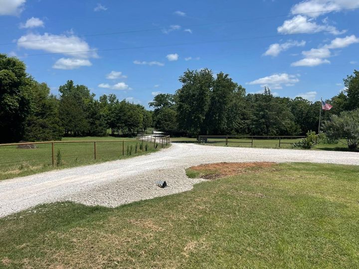 Gravel path through grassy field under blue sky with trees and a small American flag in the distance