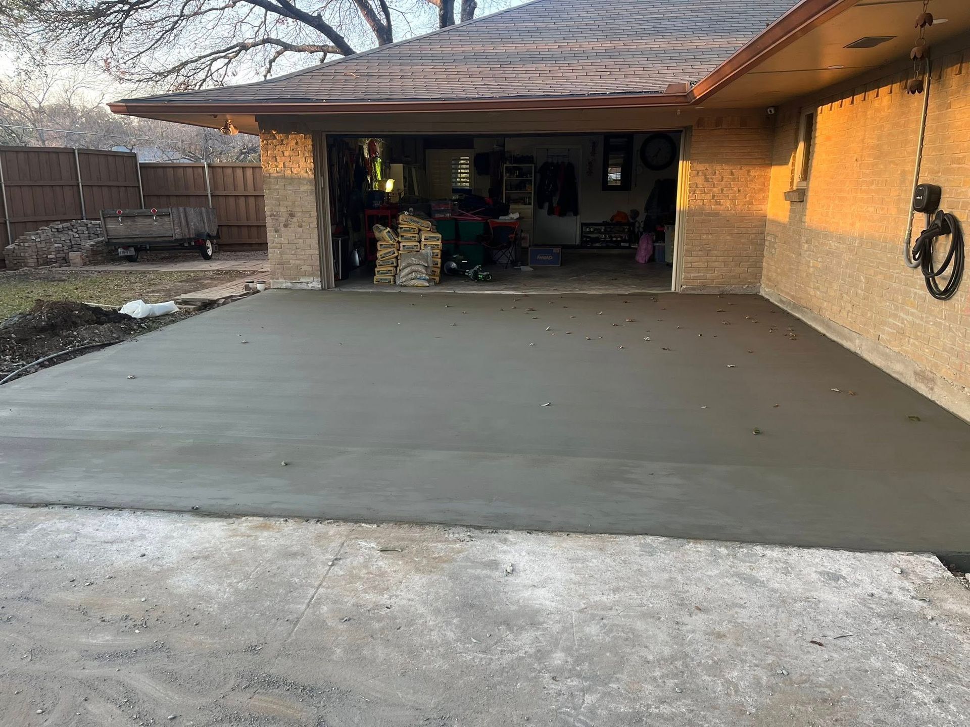 Freshly poured concrete driveway leading to an open brick garage at a house.