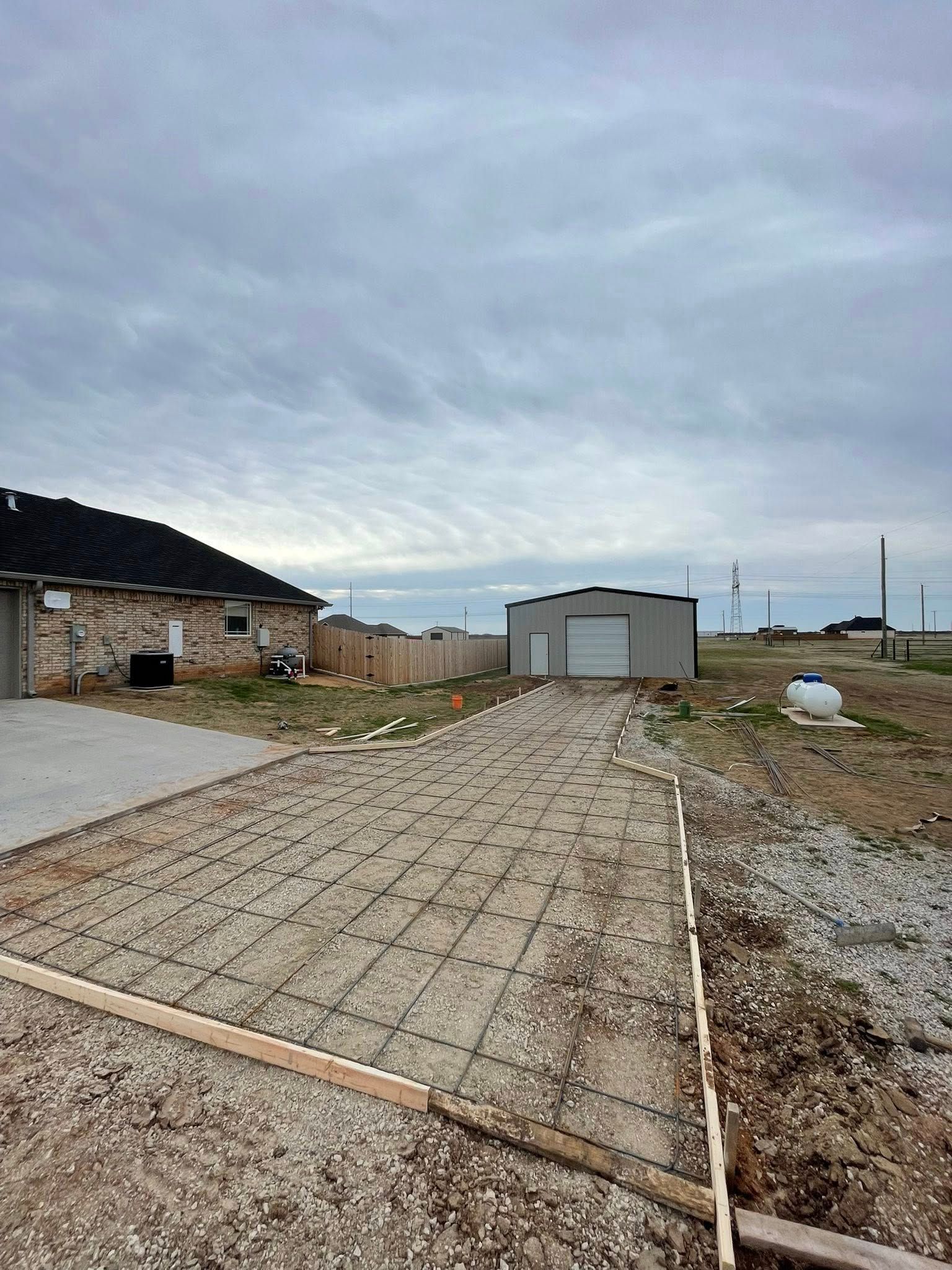 Cloudy rural driveway with stone paving, a stone house on the left, and a metal shed ahead.