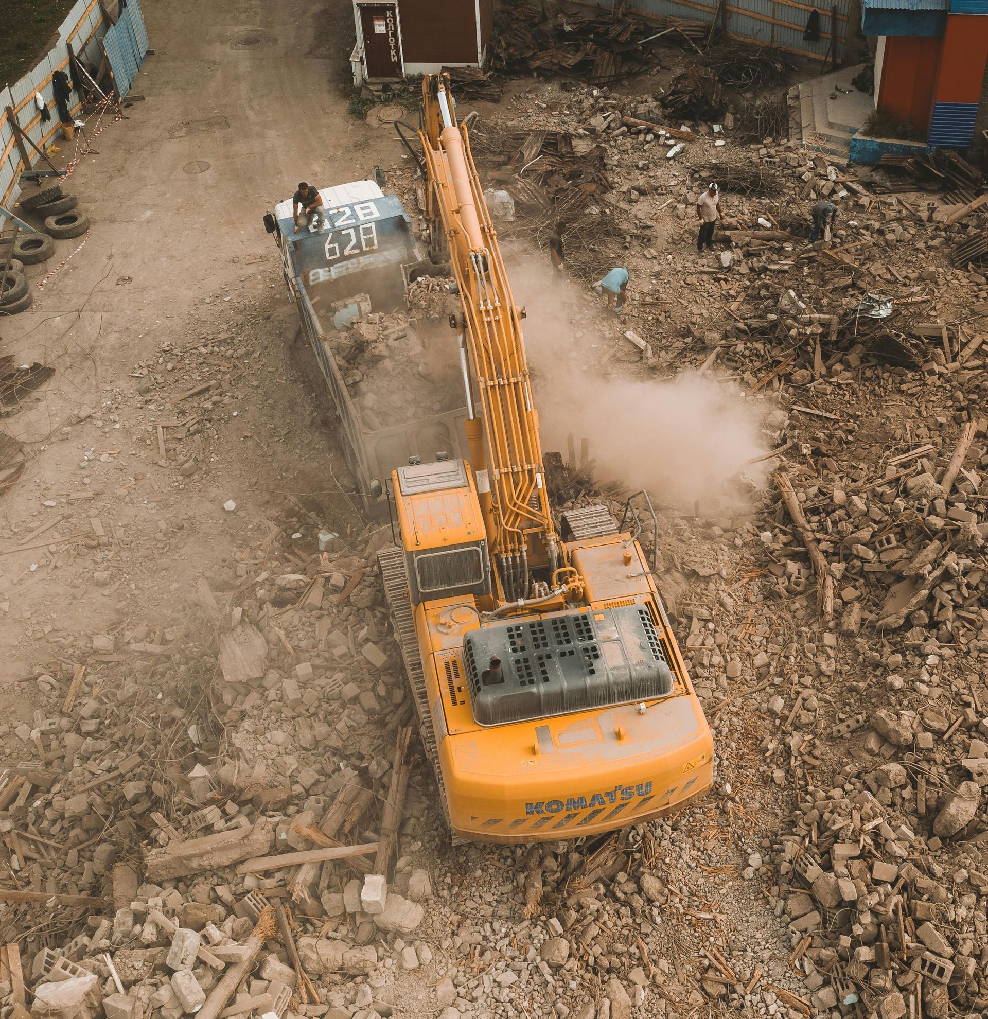 Orange excavator digging rubble in a demolition site, raising dust.