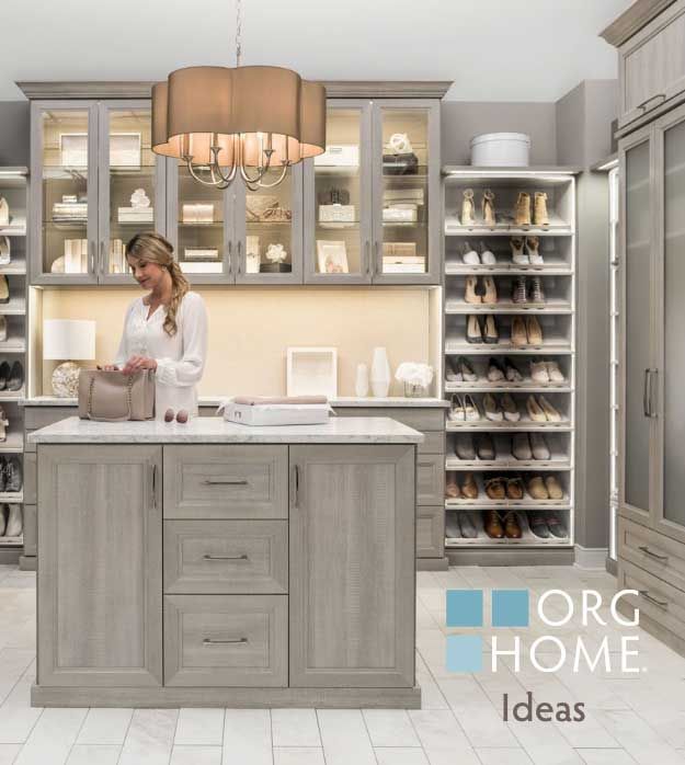 Gray kitchen with glass cabinets, island, and a person arranging items under a pendant light