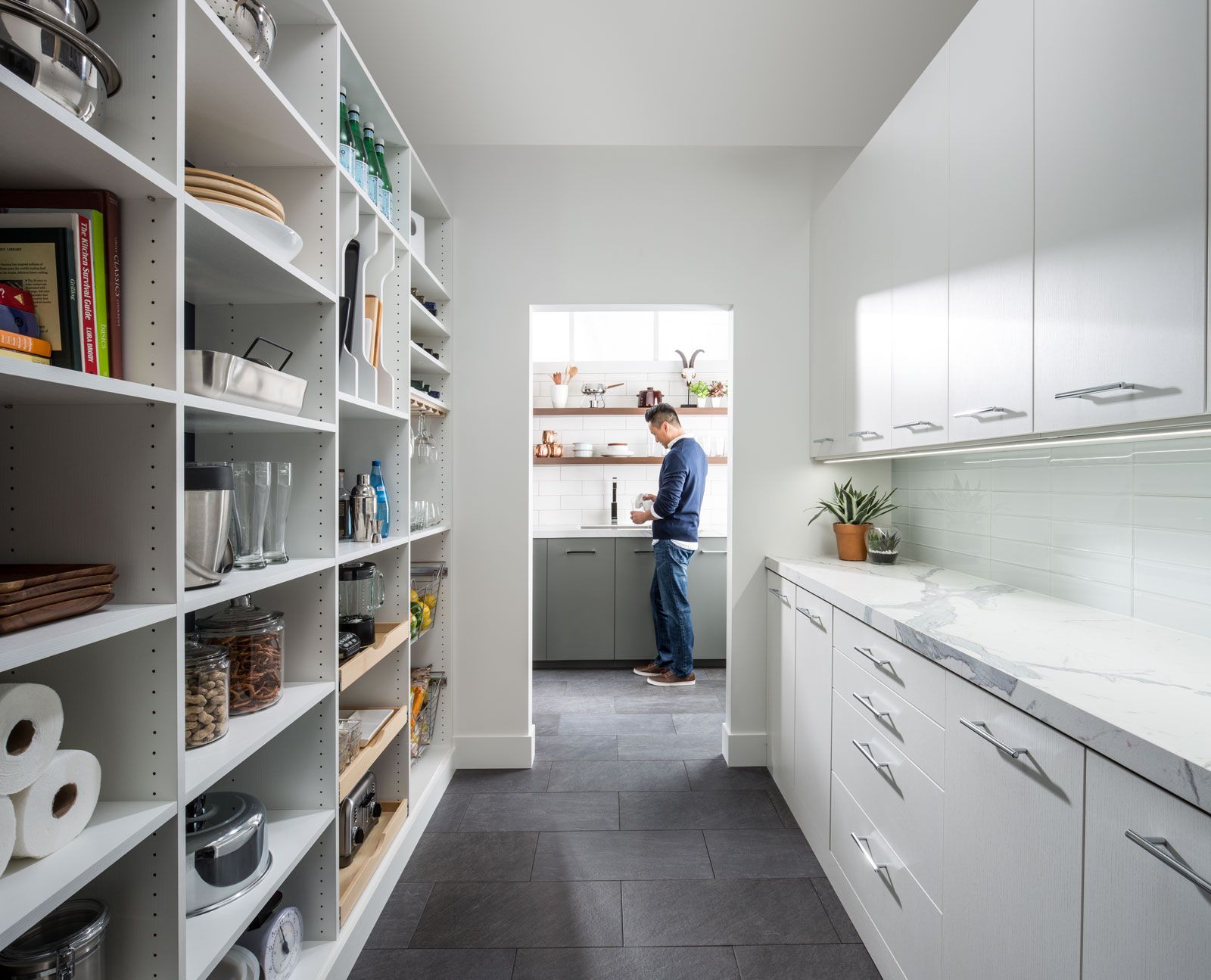 Bright walk-in pantry with shelves and white cabinets; a person stands by the window at the far end.