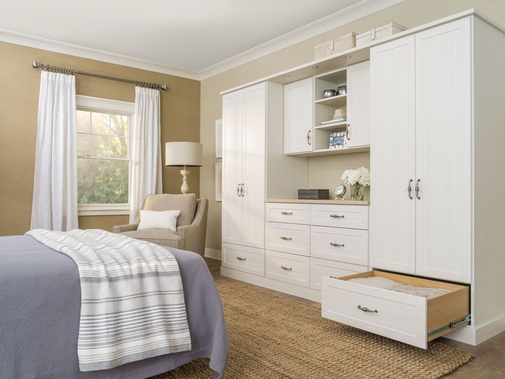 A bedroom with a bed , chair , drawers and cabinets.
