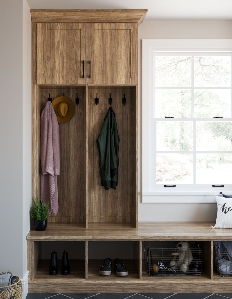 A mud room with wooden cabinets , a bench , and a window.