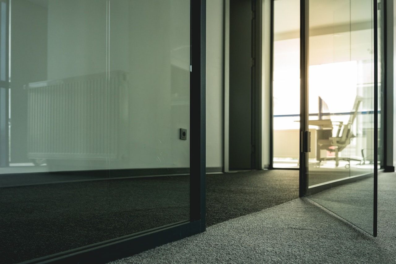 Modern glass office hallway with open doors and a table near a bright window