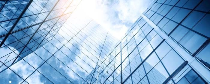 Blue-tinted glass skyscraper reflecting a bright sun and sky, viewed from below