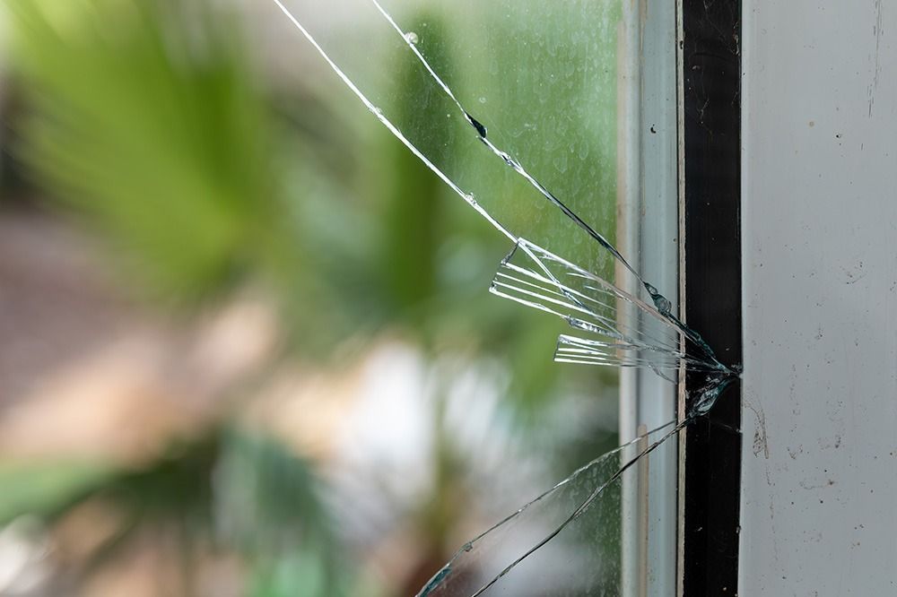 Cracked windowpane with a spider web-like fracture near the right edge, blurred green background