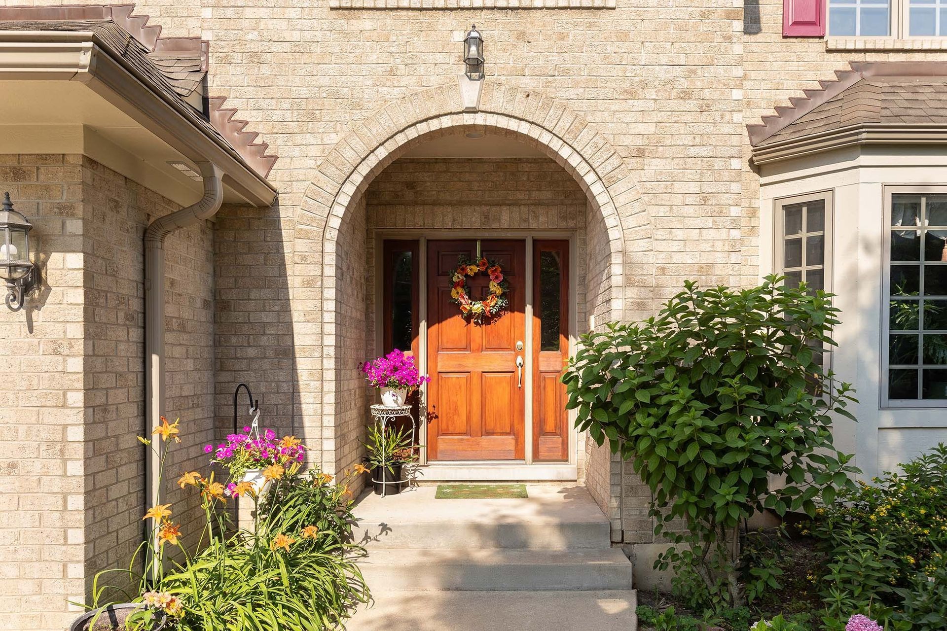Stone house entryway with an arched wooden door, potted flowers, and greenery along the walkway