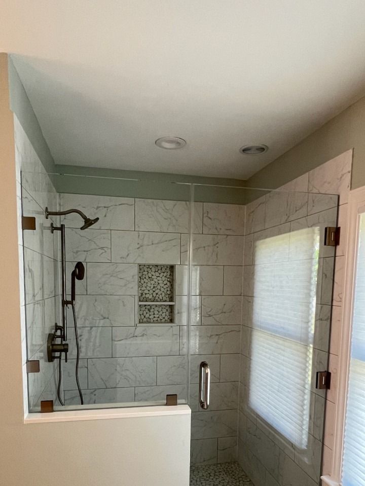 Modern tiled shower with glass door, wall-mounted showerhead, handheld sprayer, and small mosaic niche