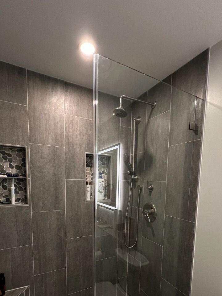 Modern tiled shower with glass enclosure and chrome fixtures in a gray bathroom