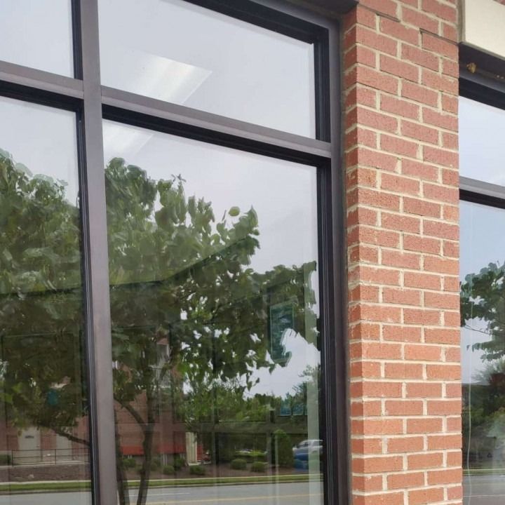 Brick building exterior with large reflective windows and a tree visible in the glass
