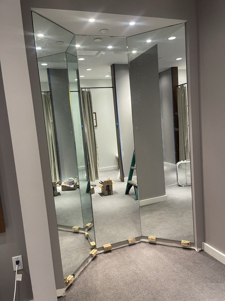 Mirrored wall panels in a carpeted room with gray walls and ceiling lights.