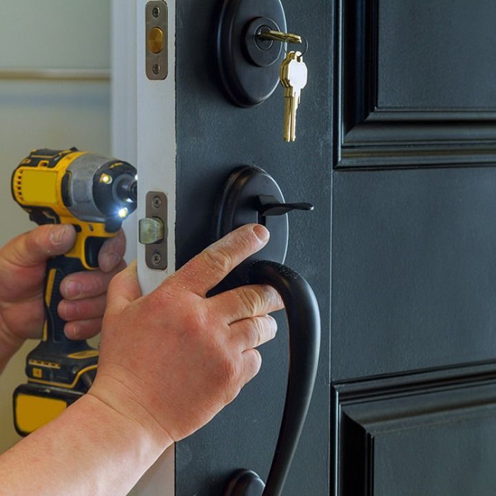 Person installing a black door handle with a yellow drill on a black front door